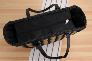 Close-up of woven straw tote bag with black leather handle and silver zipper closure