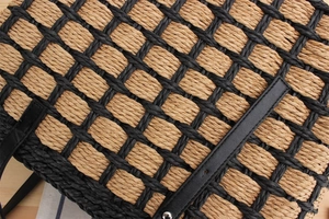 Detail of woven straw tote bag featuring contrast checkered pattern and black leather strap