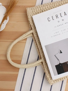 Sac de plage minimaliste en paille tressée beige avec poignées rondes sur table bois
