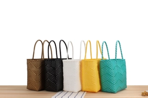 Close-up of woven tote bags in brown black white yellow and green on a wooden table