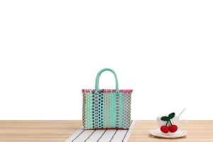 Detail of colorful plastic woven picnic basket with a soft mint green handle on wooden table