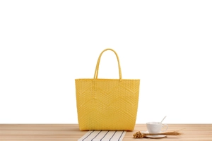 Detailed close-up of yellow woven tote bag with wavy texture on a wooden surface