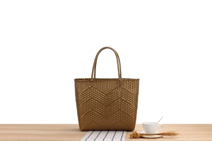 Detail of bronze woven tote bag with wave texture and round handles on a table