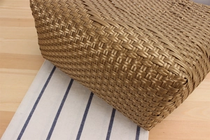 Close-up of bronze woven tote bag showing detailed herringbone texture on a desk