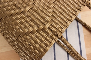 Detail of golden woven tote bag featuring metallic texture and braided handles