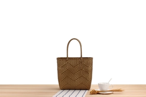 Detailed view of bronze hand-woven tote bag with wavy texture on wooden surface