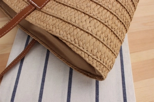 Detail of woven straw tote bag texture with brown leather strap and contrast stitching