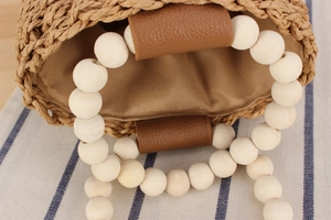 Detail der handgewebten Strohtasche mit glatten Holzperlengriffen und Lederakzenten
