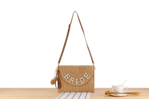 Detail of woven straw envelope bag with pearl BRIDE lettering and brown leather strap
