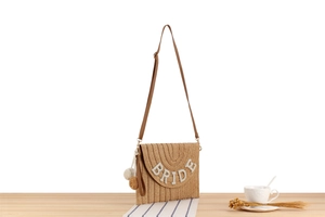 Close-up of straw woven envelope bag featuring white sequined BRIDE text and tassel