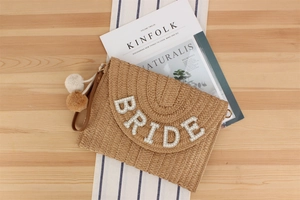 Detail of straw woven clutch bag with beaded BRIDE lettering and plush pompom charms