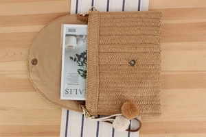 Detail of hand-woven straw envelope bag with magnetic clasp and fuzzy pom pom charms