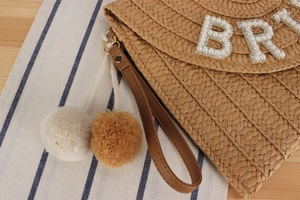 Detail of woven envelope bag with pearl BR logo, leather strap and fluffy charms