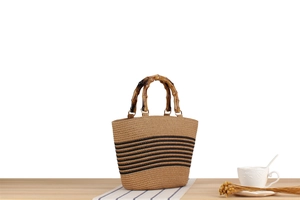 Detail of woven straw tote bag with black stripes, bamboo handle, and golden metal rings