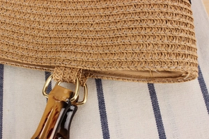 Detail of woven straw bag showing bamboo-style handle with gold metal ring connection