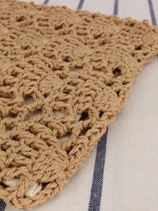 Detailed macro view of tan handmade crochet knit texture on a striped fabric background