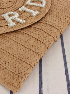 Handwoven straw envelope bag with pearl letter decor on a nautical striped background