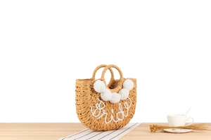 Détail du sac en paille fait main avec pompons et lettrage Bride brodé en blanc pur