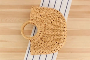 Vue à plat d'un sac à main semi-circulaire en paille sur fond de bois rustique