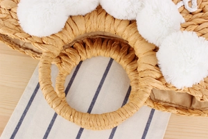 Détail d'un sac en paille tressée avec pompons blancs et poignées rondes élégantes