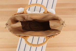 Vue de dessus du sac cabas en paille tissée avec pompons blancs et doublure à cordon