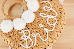 Détail du sac en paille avec pompons doux et broderie Bride en corde blanche