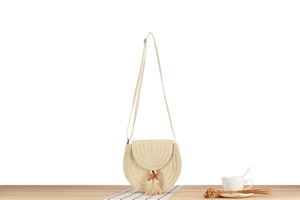 Dettaglio di una borsa a tracolla tonda in paglia con nappe colorate su legno naturale