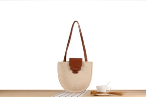 Detail of semi-circular woven bag with brown leather strap on a wooden surface