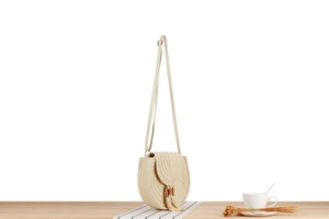 Dettaglio di una borsa a tracolla tonda in paglia con nappe su superficie di legno