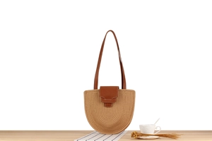 Detail of a semi-circular straw woven bag with brown leather strap on a wooden table