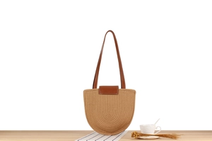Detailed view of semi-circular woven straw bag with dark brown leather straps on wood