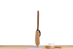 Side view of woven straw shoulder bag with brown leather strap on a wooden table