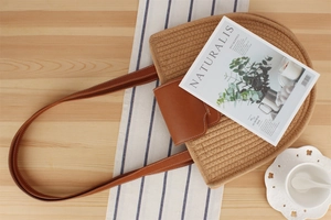 Detail of hand-woven straw tote with brown leather flap and contrast stitching accents