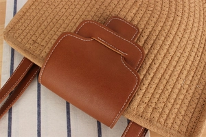 Detail shot of hand-woven straw bag with red-brown leather trim and white stitching