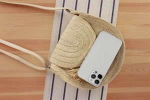 Dettaglio della borsa rotonda in paglia beige che mostra la capacità con uno smartphone
