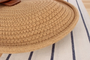 Detail of woven straw texture with brown leather stitching on a striped canvas background