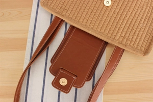 Detail of woven straw handbag featuring brown leather strap and magnetic metal closure