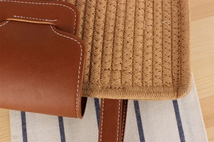 Detail of woven straw handbag with brown leather flap and white decorative stitching