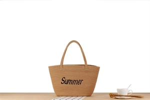Détail d'un grand sac seau en paille tissée avec broderie Summer sur surface en bois clair