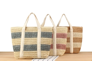 Three oversized woven paper straw tote bags with colorful stripes on a wooden surface