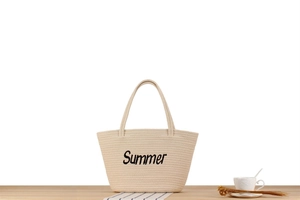 Détail de la broderie Summer sur un sac cabas tissé beige sur une table en bois