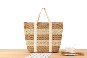 Detail of two-tone woven paper rope tote bag with wide straps on a wooden table