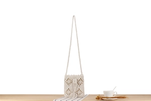 Detailed close-up of beige crochet floral handbag with woven strap and drawstring closure