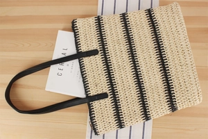 Grand sac cabas tissé beige avec rayures noires et anses en cuir sur une table en bois
