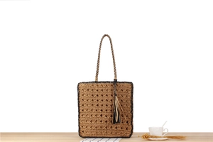 Détail d'un sac cabas tissé main avec pompons sur une table en bois clair