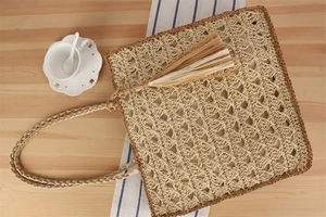 Détail d'un sac bandoulière en paille fait main avec glands sur une table en bois