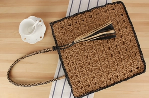 Vue à plat d'un sac en paille tissée avec pompons sur table bois et tasse café