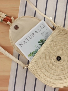 Borsa a tracolla rotonda in paglia beige con patta magnetica su tavolo di legno
