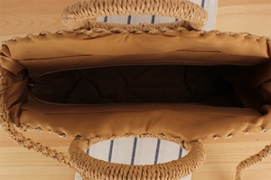 Top view of handwoven straw tote bag showing brown zipper closure and fabric lining