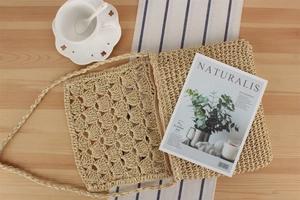 Close-up of woven straw crossbody bag with floral patterns on a wooden table setup